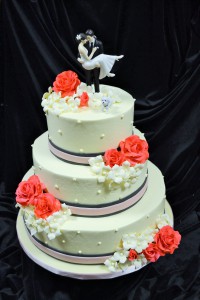 This 3-tiered wedding cake, with a pink and charcoal gray double fondant ribbon, is decorated with Swiss dots and hand-crafted coral sugar roses and ivory sugar hydrangea.