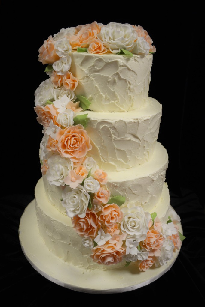 Peach and white roses and hydrangeas cascading down a 4 tiered stucco textured wedding cake